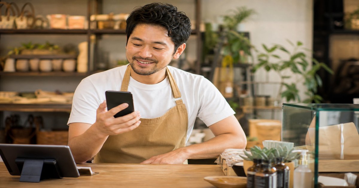 Small business owner checking Google reviews on smartphone at shop counter